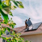 Dois profissionais instalando painéis solares no telhado, demonstrando práticas de sustentabilidade e eficiência energética em uma casa eco-friendly. A cena enfatiza a importância de energia limpa e inspirações para residências sustentáveis.