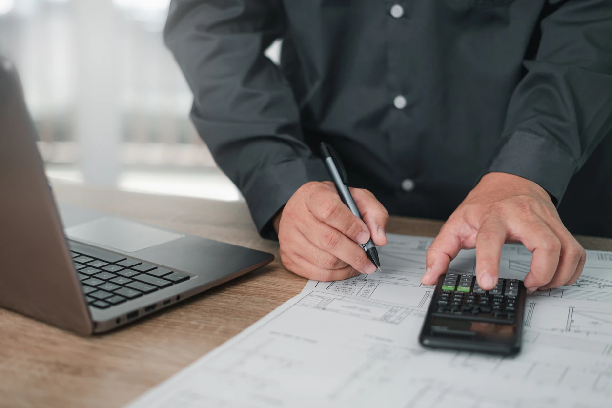 Pessoa trabalhando com laptop, calculadora e papéis em escritório moderno, focada em análise financeira ou de negócios.