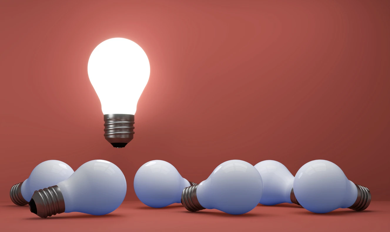 Imagem de várias lâmpadas incandescentes apagadas com uma única lâmpada acesa acima delas, simbolizando uma ideia brilhante e inovação em energia.