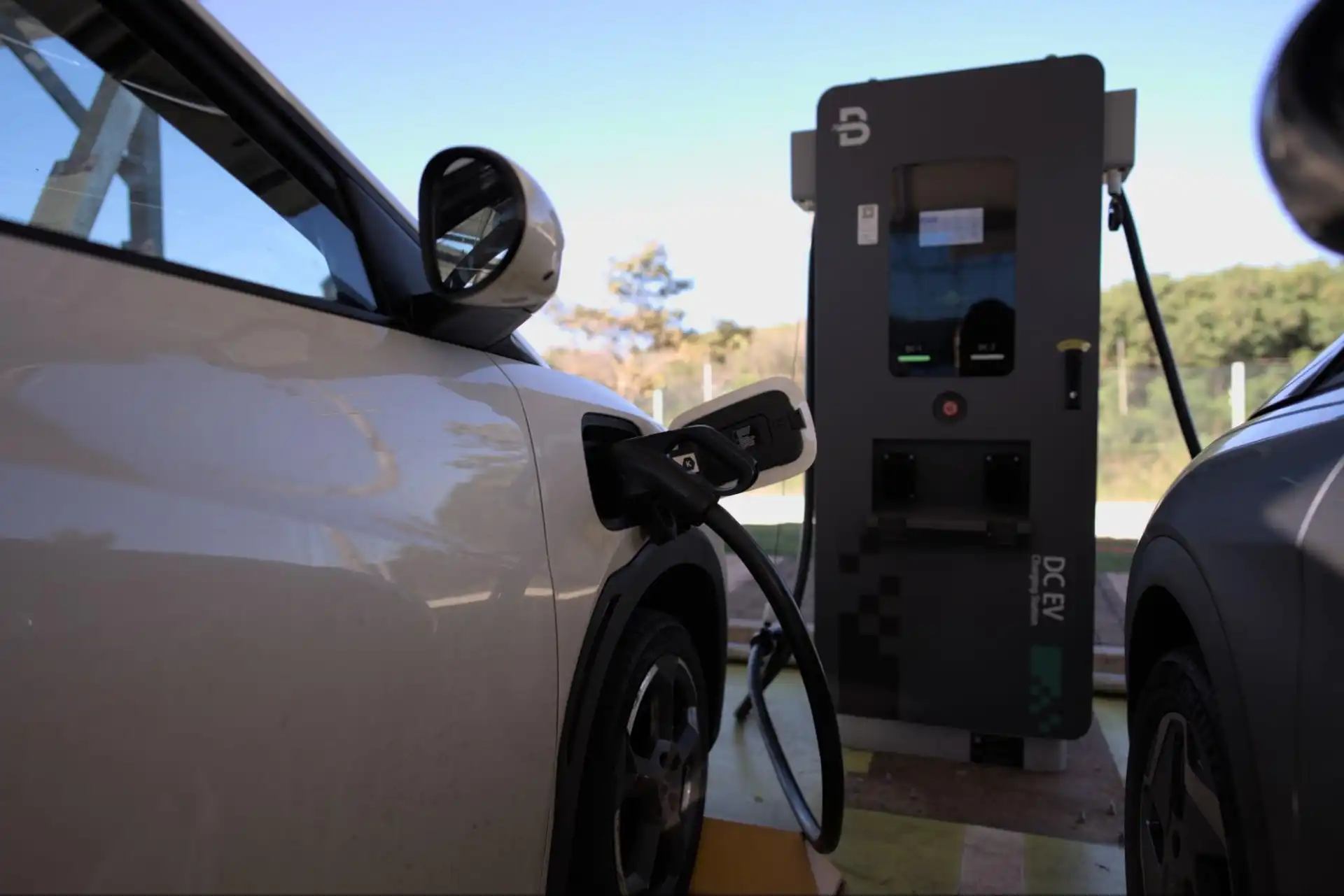 Veículo elétrico sendo carregado em uma estação de carregamento ao ar livre, com cenário de natureza ao fundo, promovendo sustentabilidade e mobilidade elétrica.